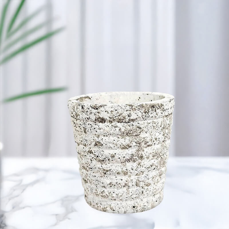 Textured ceramic planter on a white surface with a blurred plant in the background