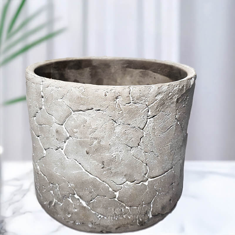 Textured gray ceramic candle pot on a white surface with a blurred green plant in the background