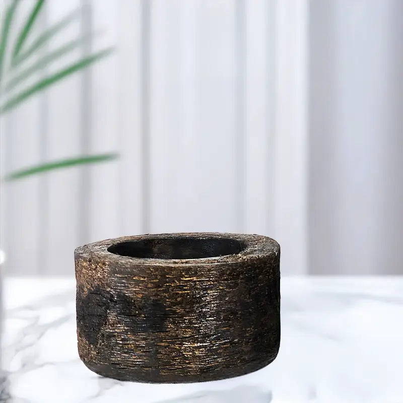 Black stone planter on a white surface with a blurred green plant in the background