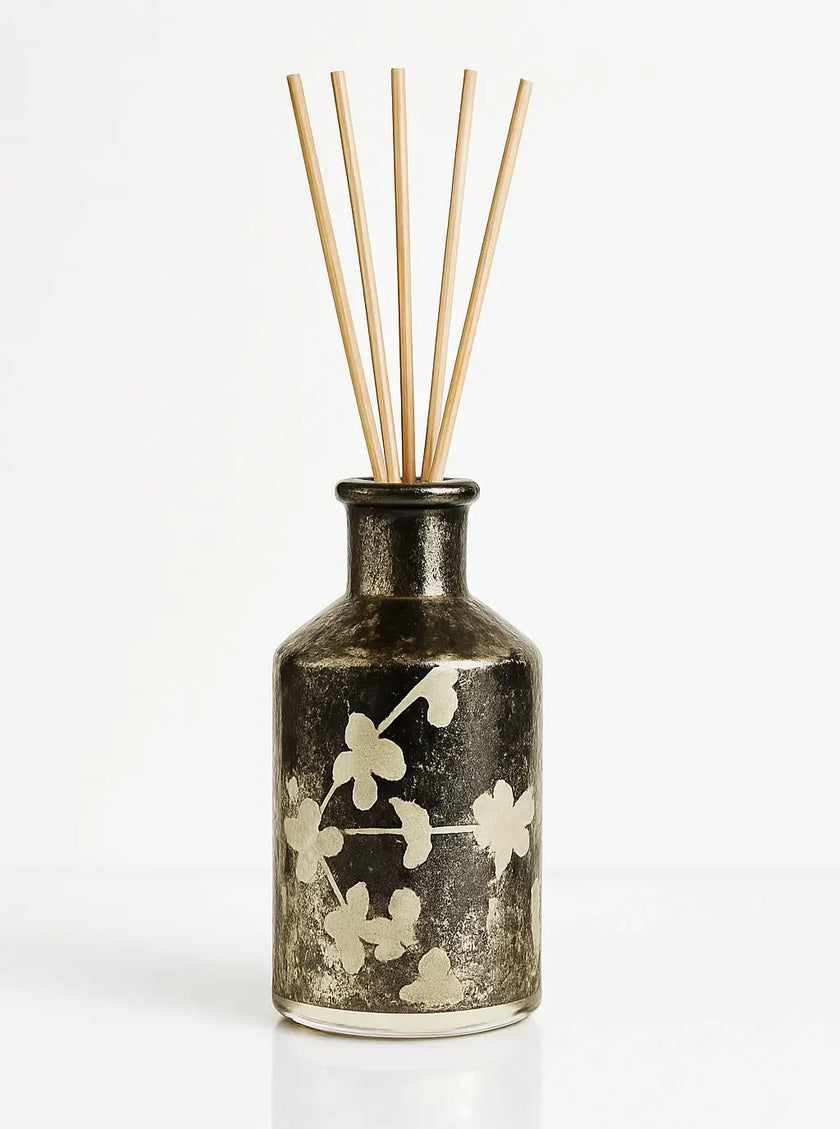 Decorative diffuser bottle with floral design and wooden sticks on a white background