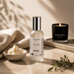 Safispa Shea Butter Body Mist bottle in a frosted glass bottle with a silver cap, styled on a marble tray with a bowl of body butter, a lit candle, and a linen cloth.