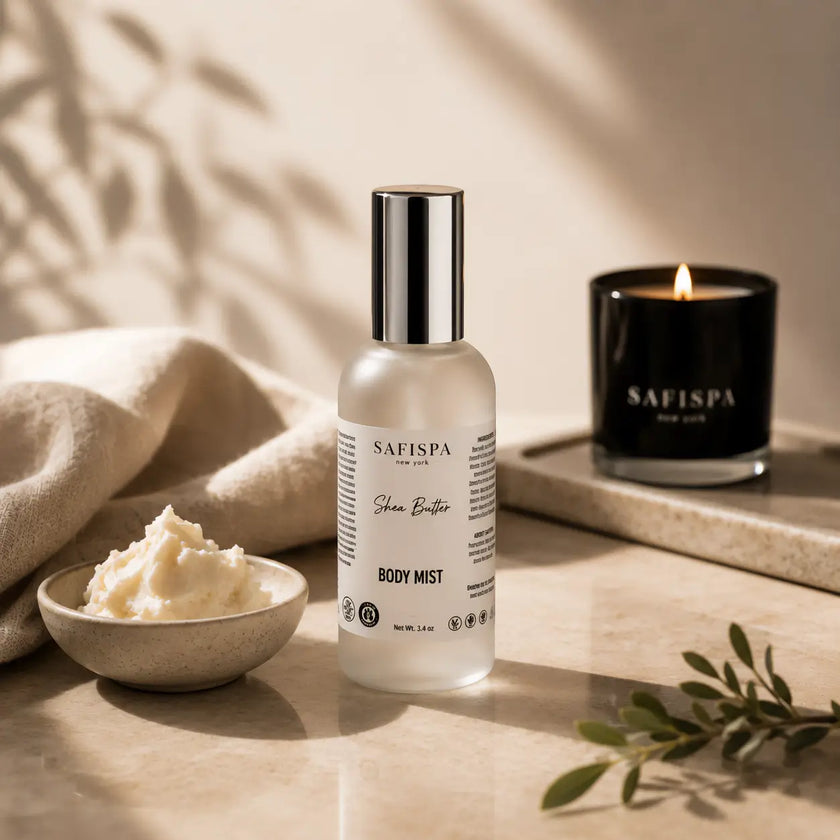 Safispa Shea Butter Body Mist bottle in a frosted glass bottle with a silver cap, styled on a marble tray with a bowl of body butter, a lit candle, and a linen cloth.