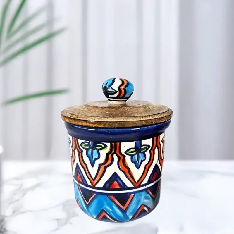 Ceramic jar with colorful geometric design and wooden lid on a white surface with a plant in the background