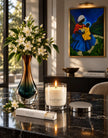 safispa jasmien marie candle in a clear glass jar sits on a dark marble table beside a tall gradient vase, matchbox, and the silver lid. 