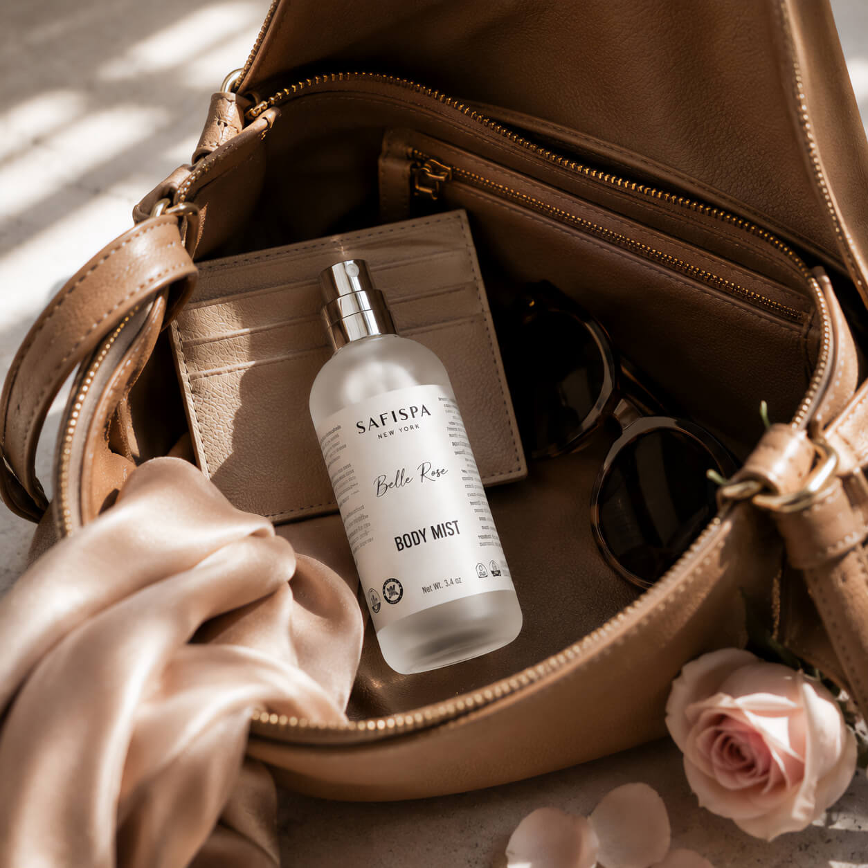 SaFiSpa Belle Rose Body Mist inside a premium leather handbag with elegant sunglasses, silk scarf, and card holder, showcasing a luxury travel-friendly rose body spray for everyday fragrance and self-care.