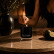 Woman lighting a SaFiSpa Ebony Bergamot candle in black glass with fresh bergamot