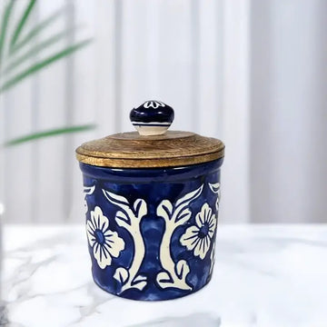 Blue ceramic jar with white floral patterns and a wooden lid on a white surface.