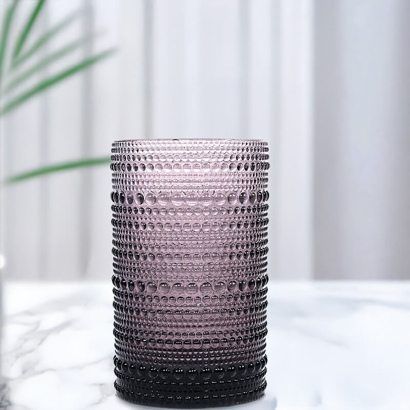 Textured purple vase candle on a white surface with a blurred plant in the background