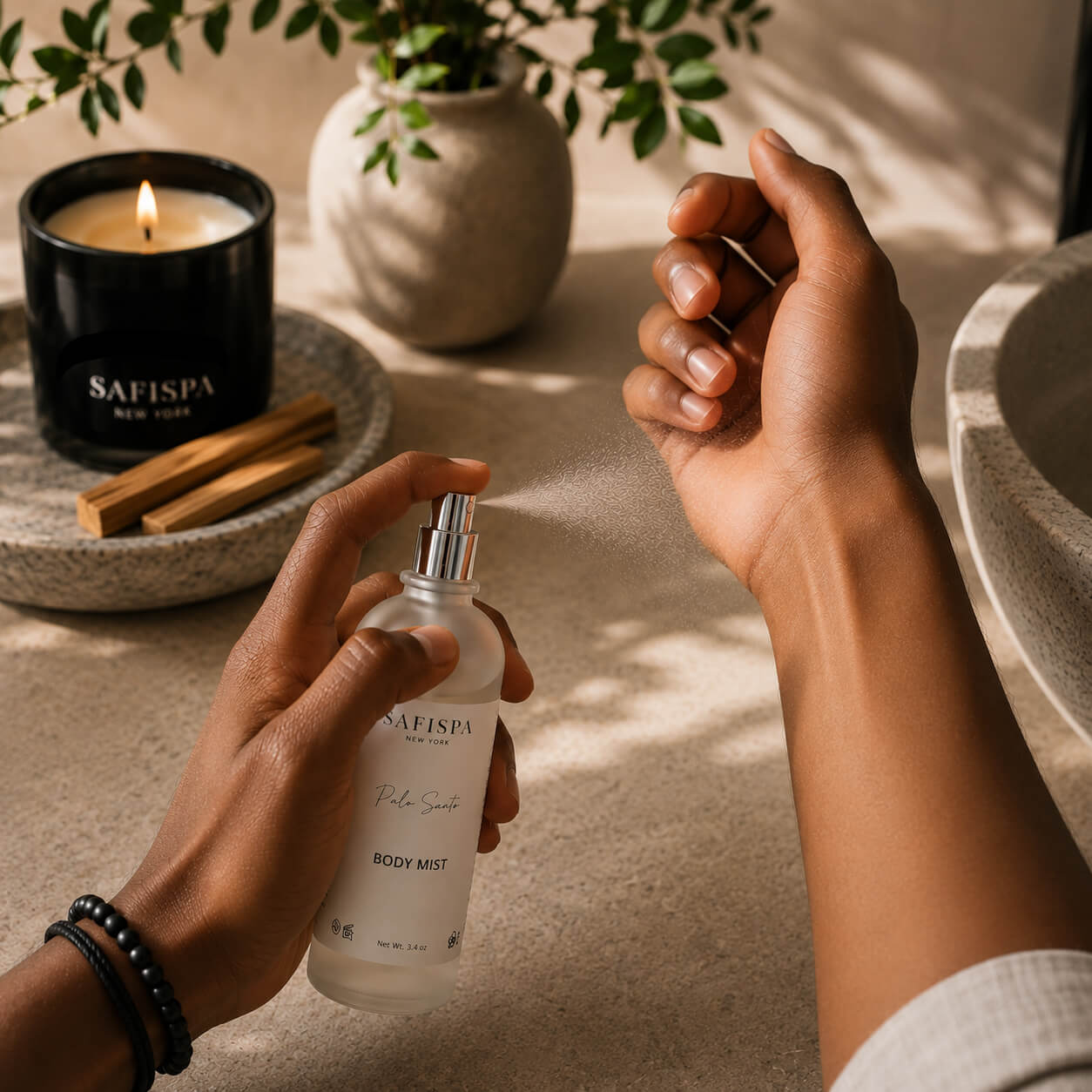 Adult applying SaFiSpa Palo Santo Body Mist to the wrist in a luxury spa-inspired setting with a lit candle, showcasing a unisex woody body spray for everyday self-care, refreshing fragrance, and clean modern grooming.