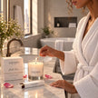 Woman lighting a SaFiSpa Belle Rose scented candle beside a pink rose in an elegant luxury home setting