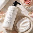 Rich cream texture of SaFiSpa Belle Rose Hand & Body Moisturizing Lotion displayed beside the luxury lotion bottle on a marble surface with fresh rose petals. Handcrafted in New York with shea butter, aloe vera, jojoba oil, coconut oil and vitamin E to deeply moisturize and soften dry skin.