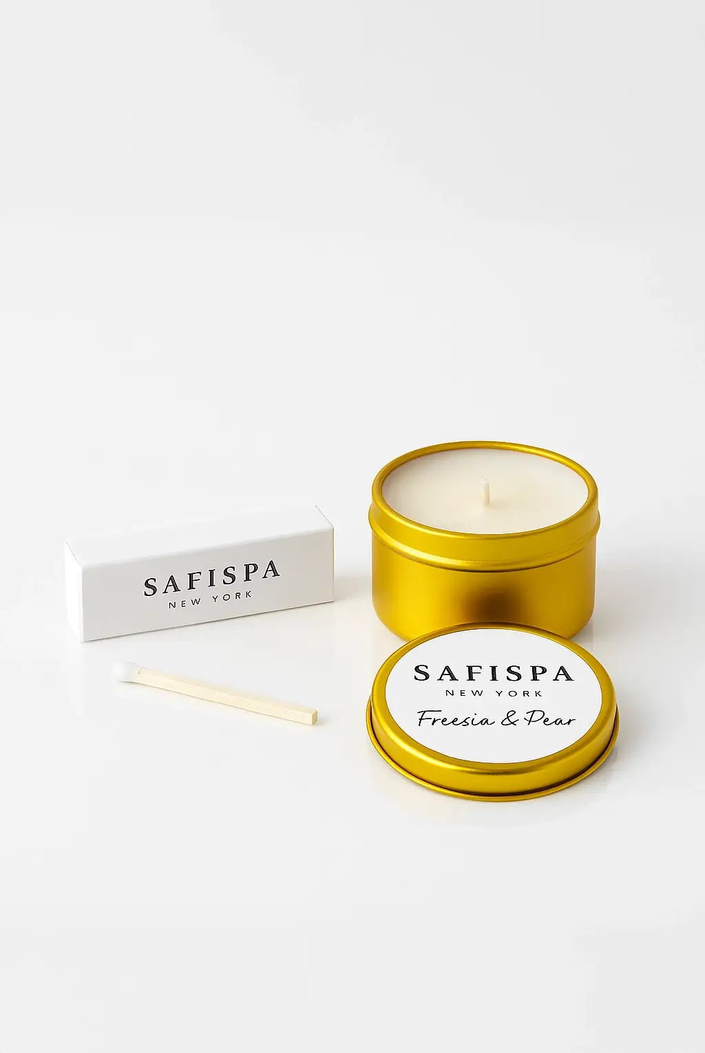SaFiSpa Freesia & Pear gold travel candle beside a white SaFiSpa matchbox on a glossy white background, luxury holiday gift set