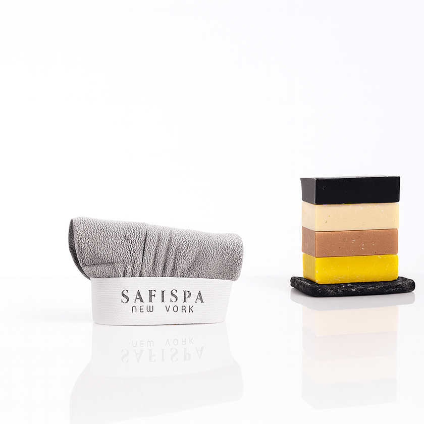  gray exfoliating towel with logo and stacked handmade artisanal soaps on a glossy white background, perfect for spa and skincare routines.