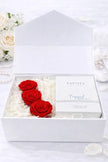 White box with red roses and a product inside, surrounded by white flowers.