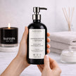Hand dispensing SaFiSpa sandalwood vetiver lotion from black pump bottle showing smooth moisturizing cream