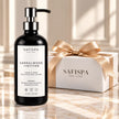 SaFiSpa Sandalwood + Vetiver Hand & Body Moisturizing Lotion, 16 oz, in a black pump bottle beside a white luxury gift box with champagne satin ribbon.