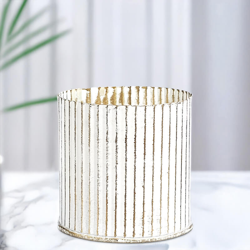 Decorative cylindrical candle bespoke container with ribbed texture on a white surface with a blurred plant in the background